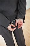 Rear view of businessman standing with handcuffs while standing on hardwood floor