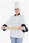 Portrait of happy woman in chef clothing holding rolling pin isolated over white background