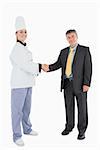Full length portrait of businessman and female chef shaking hands against white background