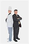 Full length portrait of businessman and female chef standing back to back against white background