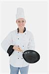 Portrait of happy female chef holding empty frying pan over white background