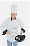 Female chef holding frying pan and spatula over white background