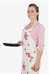 Portrait of beautiful woman in apron holding frying pan against white background