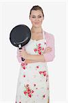 Portrait of beautiful young woman with arms crossed holding frying pan over white background