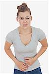 Portrait of unhappy young woman suffering from stomach pain against white background