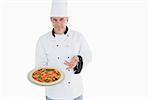 Portrait of confident chef displaying pizza over white background