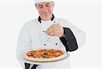 Happy male chef garnishing pizza with coriander leaves against white background