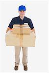 Portrait of mature courier man carrying stack of cardboard boxes against white background