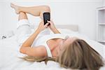 Calm woman looking at her phone lying on the bed