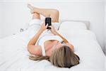 Calm woman touching her phone lying on the bed