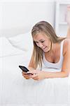 Blonde woman using her phone lying on the bed in the bedroom