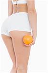 Rear view of woman in shorts with fresh orange over white background