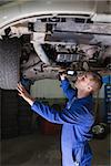 Male mechanic examining car using flashlight in garage