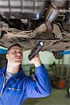 Male mechanic with flashlight examining under car