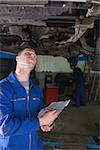 Mechanic examining under car as he prepares checklist