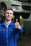 Portrait of happy car mechanic gesturing thumbs up in workshop