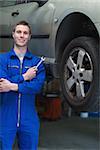 Portrait of young male mechanic with spanner standing by car