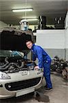 Portrait of male mechanic examining car engine in workshop