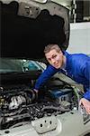 Portrait of male mechanic working under bonnet of car