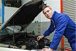 Portrait of confident male mechanic checking car engine oil