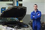 Portrait of confident mechanic standing by car with open hood