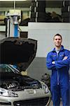 Portrait of confident male mechanic standing by car with open hood