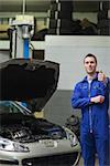 Portrait of male mechanic by car with open hood gesturing thumbs up