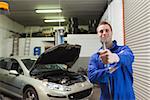 Portrait of young male mechanic offering spanner in worshop