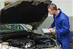 Male mechanic with clipboard examining car engine