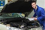 Portrait of male mechanic with clipboard analyzing car engine