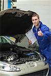 Portrait of male mechanic by car with open hood showing thumbs up