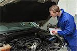 Male mechanic writing on clipboard while examining car engine