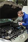 Auto mechanic writing on clipboard while examining car engine