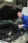 Portrait of auto mechanic with clipboard examining car