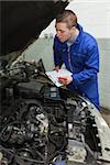 Mechanic preparing checklist while looking at car engine