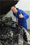 Portrait of confident mechanic by car with open hood gesturing thumbs up