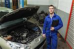 Portrait of male mechanic standing by car with open hood