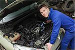 Portrait of male mechanic with flashlight examining car engine