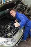 Portrait of auto mechanic by car showing thumbs up sign