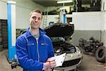 Portrait of male mechanic writing on clipboard in workshop