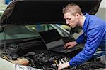 Car mechanic with laptop repairing engine