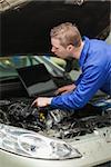 Male repairman with laptop checking car engine
