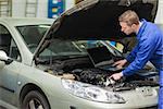 Male mechanic with laptop checking car engine