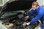 Male mechanic with laptop repairing car engine in workshop