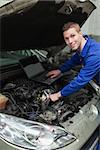 Portrait of happy mechanic with laptop repairing car engine