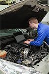Male mechanic using laptop while repairing car engine