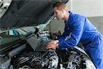 Auto mechanic by car working on laptop