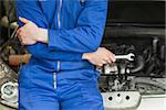 Male mechanic in coveralls leaning on car