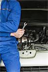Male mechanic with spanner leaning on car