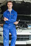 Portrait of happy mechanic leaning on car engine